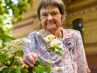 A woman stands in the hospice garden holding a flowering shrub.