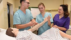 Nursing students practise on a mannequin in a hospital bed.