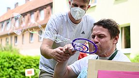 Man blowing soap bubbles, an employee assists him in holding the wand.