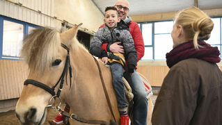 Jonas and his father smile into the camera while sitting on the horse. 
