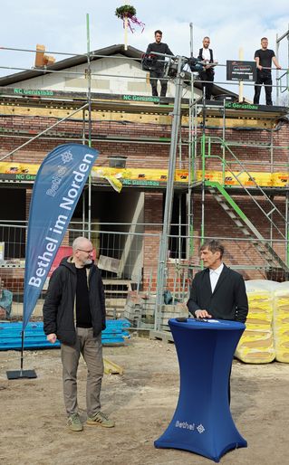 Frank Simon und Thorsten Nolting stehen am Rednerpult. Im Hintergrund sieht man den Neubau mit Richtkranz.
