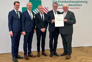 Fünf Männer lächeln und halten einen Förderbescheid.