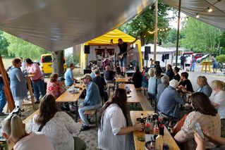 Menschen sitzen im Biergarten und hören der Band zu.