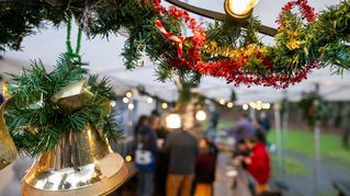 Im Vordergrund hängt Weihnachtsdeko an einem Zweig, im Hintergrund sieht man Menschen auf einem Weihnachtsmarkt