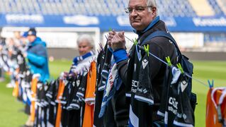 Rainer Wollenburg ist bei einer Fan-Aktion seines Fußballvereins dabei und hält eine Wäscheleine mit limitierten Trikots hoch, die später in Bethel verlost werden. 