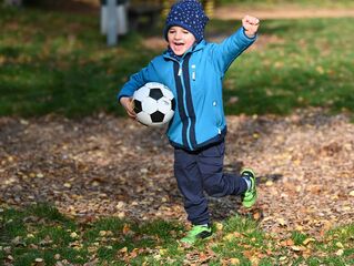 Junge mit Fußball im Arm läuft über Spielplatz