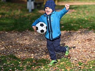Junge mit Fußball im Arm läuft über Spielplatz