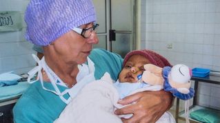 Klaudia Nußbaumer trägt eine OP-Schwester-Kleidung und hält ein Baby im Arm.