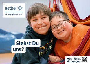 Plakatmotiv: Lukas und Max stecken die Köpfe eng aneinander und lächeln in die Kamera. Oben links steht das Bethel-Logo und unten links der Claim "Siehst Du mich?"