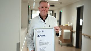 Univ.-Prof. Dr. Thomas Vordemvenne steht im Krankenhausflur und hält das eingerahmte Zertifikat in den Händen.