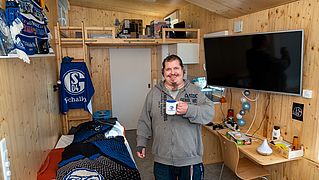 Mike Ertel steht mit einer Tasse in seinem Wohnzimmer