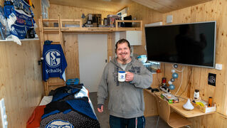 Mike Ertel steht mit einer Tasse in seinem Wohnzimmer