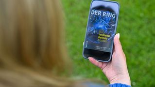Eine Person sitzt draußen und hält ein Smartphone mit der digitalen Ausgabe von DER RING in den Händen