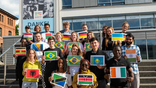 Internationale Bethjahrteilnehmerinnen und Teilnehmer halten ihre Landesfahnen in die Kamera