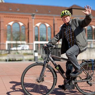 Mann sitzt auf dem Fahrrad und winkt.