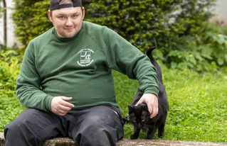 Ein Mann sitzt neben einer Katze und streichelt sie.