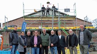 Gruppenbild vor dem Neubau mit Baugerüst und Richtkranz.