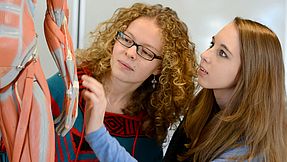 Two schoolgirls look with interest at an anatomical muscle model.