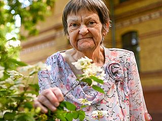 Frau steht im Garten des Hospizes und hält einen blühenden Strauch in der Hand.