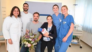 Gruppenbild mit Eltern und Baby sowie Klinikpersonal.
