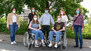 Im Vordergrund sitzen zwei Personen im Rollstuhl. Dahinter stehen fünf Personen.