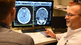 A doctor and a man sit in front of an MRI image and talk to each other.