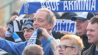 Fans aus Bethel bejubeln im Publikum mit Vereinsschalen Arminia Bielefeld.