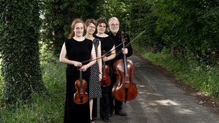 Musikerinnen und Musiker stehen mit ihren Instrumenten im Grünen.