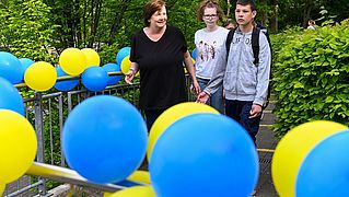 Lehrerin führt Jungen über mit Luftballons geschmückten Hof zum Schulgebäude