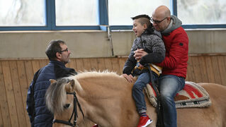 Marco Vohmann spricht mit Jonas, der mit seinem Vater auf dem Pferd sitzt.