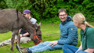 Stefan Simon takes a break and sits in a meadow with Gisela Krohn, holding the donkey by the rope. 