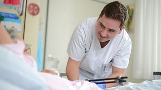 Ein Pfleger beugt sich lächelnd zu einem Patienten