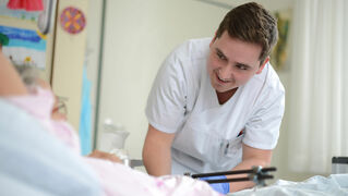 Ein Pfleger beugt sich lächelnd zu einem Patienten