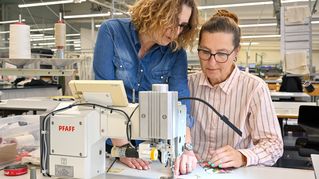 Eine Frau leitet eine andere Frau an der Nähmaschine an.