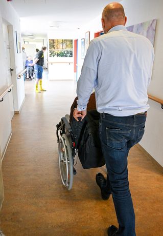 Pastor Dr. Bartolt Haase schiebt einen Mann im Rollstuhl über den Flur.
