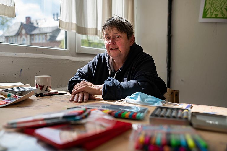 Susanne Hadamitzky sitzt im Atelier. Vor ihr liegen Stifte in vielen Farben.