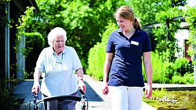 Carer accompanies senior citizen outside.