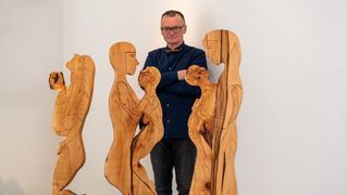 Sergej Ratke vor Holzskulpturen in Form von Menschen