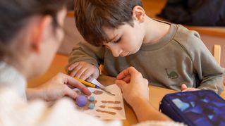 Eine Frau hilft einem Jungen beim Basteln.