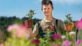 Ein junger Mann arbeitet in der Gärtnerei Bethel und hält zwei Blumen in die Luft.