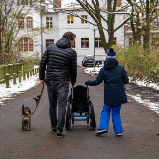 Christian Götze geht mit Artem spazieren. Beide schieben einen Rollstuhl. An der Leine läuft ein Hund.