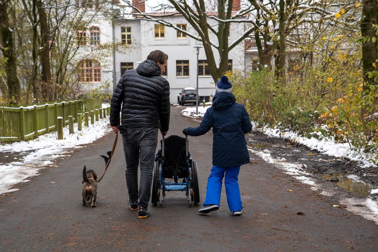 Christian Götze geht mit Artem spazieren. Beide schieben einen Rollstuhl. An der Leine läuft ein Hund.
