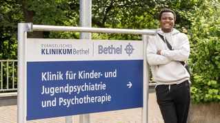 Ein junger Herr steht neben einem Schild - Krankenhausbeschilderung 