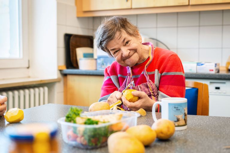 Christa Feld schält Kartoffeln und lächelt dabei in die Kamera.