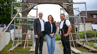 Bethels Vorstandsvorsitzender Pastor Dr. Bartolt Haase (v.l.), Linda Bulthaup aus der Direktion der Bethel-Stiftungen Sarepta und Nazareth, und Manuel Hüls, Geschäftsführer von Tragwerk Holzbau e.K., vor dem aufgestellten Torbogen am Quellenhofweg.