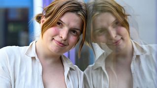Alicia Lütze leht an einer Scheibe und schaut in die Kamera. Ihr Gesicht spiegelt sich im Glas.