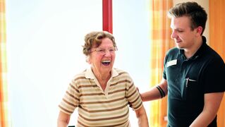 A carer supports a smiling elderly woman