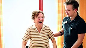 Pfleger unterstützt Seniorin beim Laufen.
