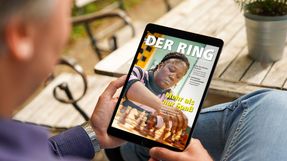 Eine Person sitzt an einem Tisch und hält ein Tablet mit der digitalen Version von DER RING in den Händen.