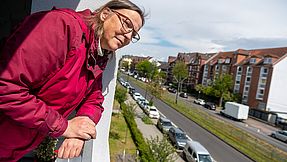 Frau schaut von ihrem Balkon herunter auf eine Straße.